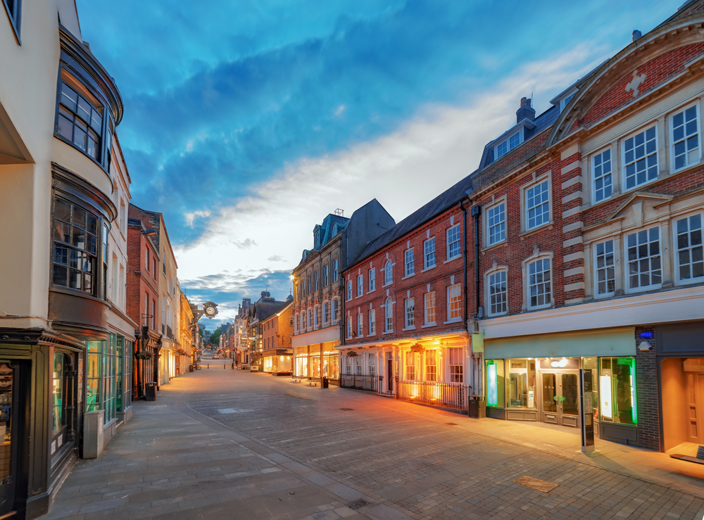 An image of a high street in an unknown town, it's twilight and the shop entrances are lit