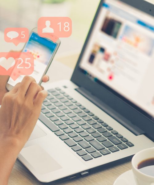 A laptop set up on a white table with a mug of black coffee, there is also a mobile phone showing likes on Instagram