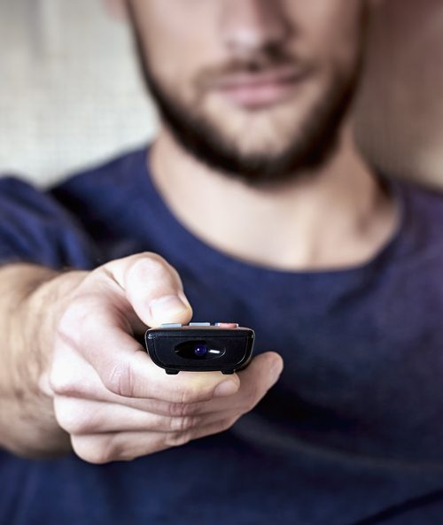 bearded man holds a remote control towards the screen
