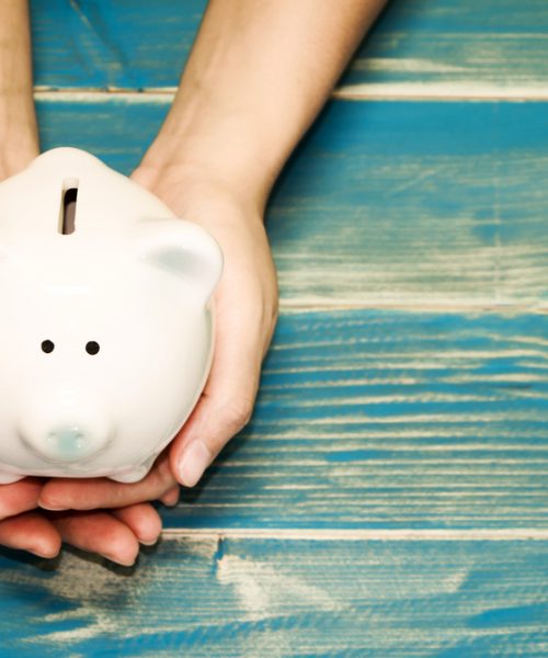Hands holding a piggy bank on a blue table