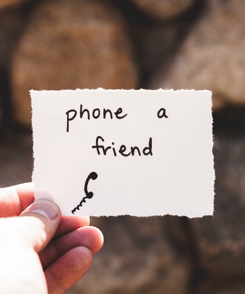 A hand holds a small piece of paper saying the words phone a friend
