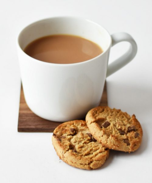 A white mug containing tea with two chocolate chip cookies sit in front