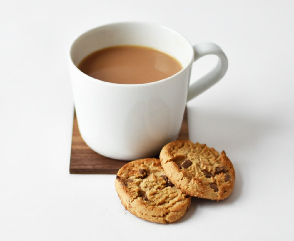 A white mug containing tea with two chocolate chip cookies sit in front