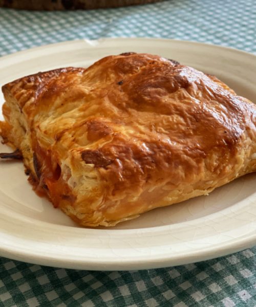 A folded pastry parcel filled with baked beans and sausages on a white plate with a green checked table cloth