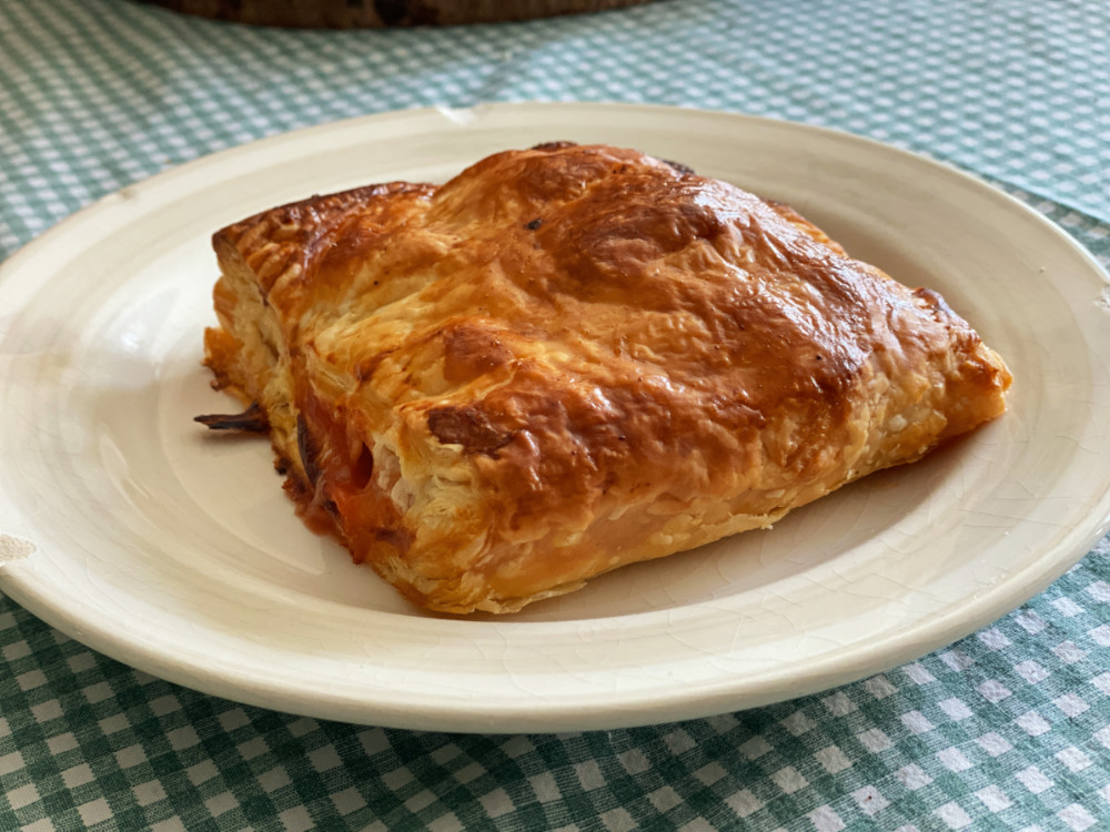 A folded pastry parcel filled with baked beans and sausages on a white plate with a green checked table cloth