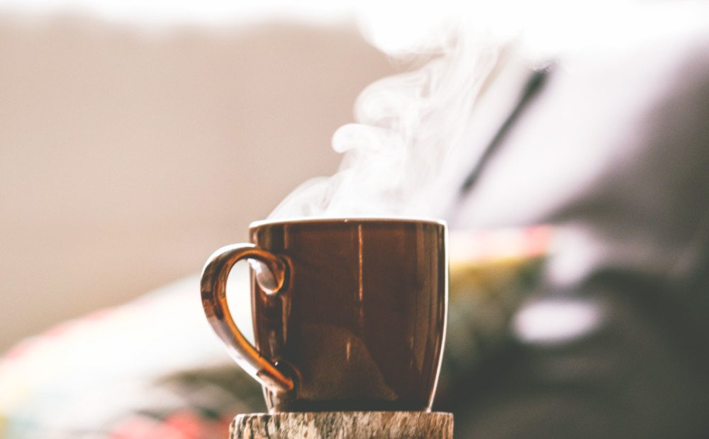 A brown metallic mug with steam coming out of it, with a slightly blurred background