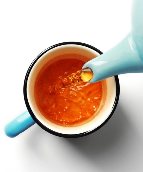 A blue teapot tipped and pouring tea into a matching tea cup